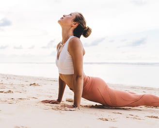 A woman practicing yoga on the beach - Holistic Health Company