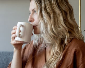 a woman with blonde hair and a brown shirt is drinking a cup of coffee