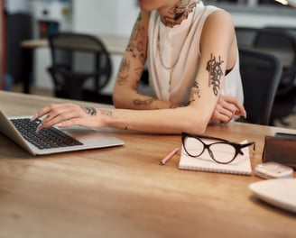 tattooed woman scrolling laptop