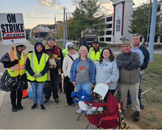 Large group of people standing with a on strike sign