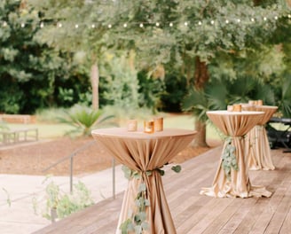 Mesa de coctel para eventos en el patio de una casa, decorada con manteles y veladoras