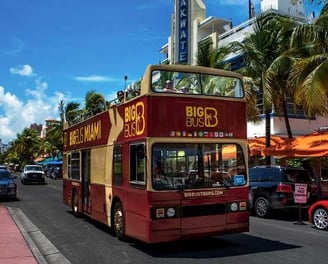 a red double decker bus driving down ocean drive