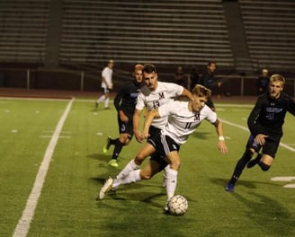 College soccer players competing on a field, one dribbling the ball