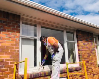 a man in a orange shirt and white pants is painting a window