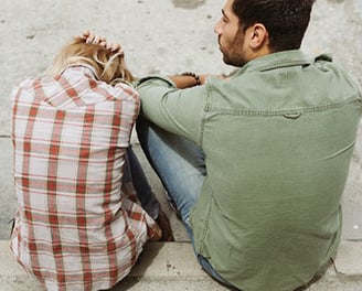 Una pareja hombre y mujer, sentados en el suelo, después de discutir