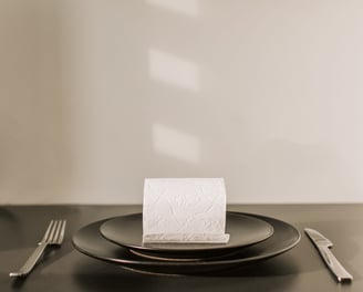 Rollo de papel higiénico, servido sobre un plato y cubiertos al lado