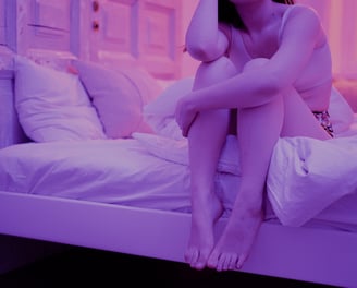 Mujer sentada en la cama, en habitación con tonalidades moradas