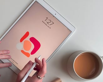 Person doing design work on a tablet, cup of tea next.  Represents branding and design.