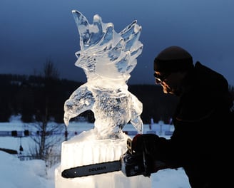 Man with cutting tool carves large wooden bird