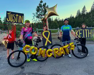 A group of people with balloons and a congrats sign with two cyclists