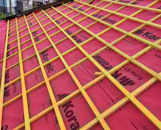 Installation de liteaux et d’un écran de sous-toiture rouge pour préparer la pose des tuiles, sur un chantier de rénovation à