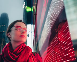 a woman in a red scarf and glasses next to led screen