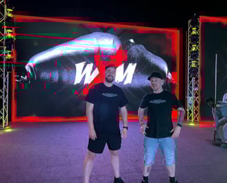 Two men stand in front of an LED screen at a wrestling show.