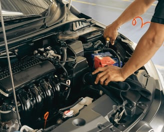 Mechanic connecting electrical wires under the hood for car repairs and diagnostics.