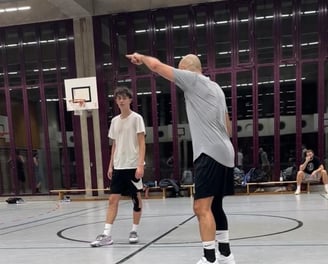 alt="Basketballtrainer gibt Anweisungen an Jugendspieler im Training."