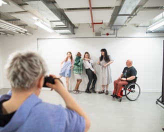 Four standing people of various ethnicities and a manual wheelchair user being photographed