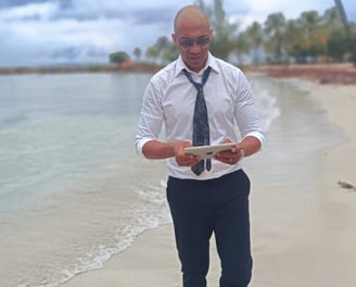 « Bruno Valery en réflexion stratégique, tablette en main, marchant sur une plage paradisiaque en Guadeloupe »