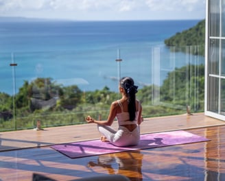 a woman sitting on a yoga mat in front of a large window