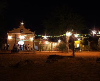  Igreja iluminada com bandeirolas e pessoas reunidas na Festa de São João à noite