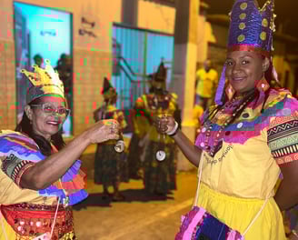 Ciganinhas sorrindo e dançando à noite com trajes coloridos e coroas em celebração quilombola