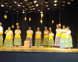 Ciganinhas se apresentam em palco com saias coloridas, turbantes e iluminação cênica