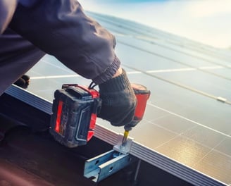 un technicien entrain de fixer des panneaux solaires sur un toit avec une viseuse professionnelle