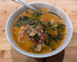 A photo of a bowl of soup, containing ground turkey, kale, tomatoes, and white beans