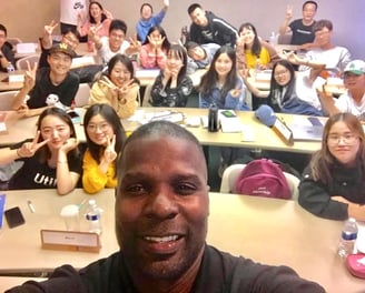 Dr. Marlon Ware standing in front of his class with students holding up the peace sign