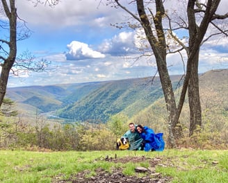 a couple with dog hiking and sitting on a mountain top peak