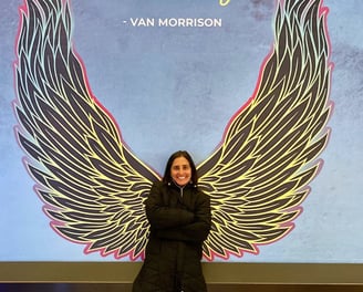 a woman standing in front of a large poster with angel wings and Van Morrison quote "Smell the sea"