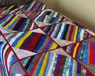 A twin-sized bed with a grey striped quilt featuring multicolored accent stripes, a gift for son