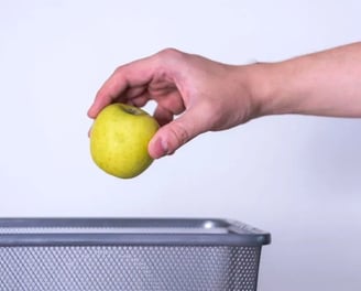 Hand tossing spoiled apple into trash can