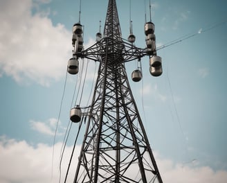 Multiple telecommunications towers rise against a backdrop of a cloudy sky. The towers are tall and metal, equipped with various antennas and satellite dishes. The scene suggests a rural or remote setting with a focus on the technology infrastructure.