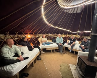 Photo of mens group with six men taking place in a yurt with wood stove