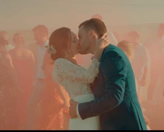 Baiser des mariés capté au milieu d’un décor coloré et vivant avec les invités en mouvement