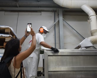 una joven filmando a un operario en una fábrica