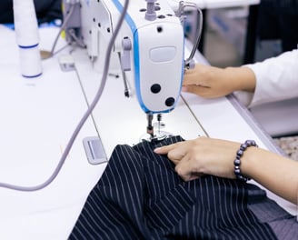 Señora cosiendo con una maquina de coser una tela azul con rayas blancas
