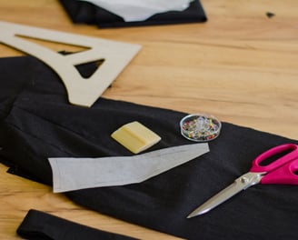 Trozo de tela, patron de ropa, unas tijeras y unos alfileres sobre una mesa de madera
