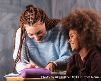 Smiling woman helping a young girl with schoolwork in a warm, supportive setting.