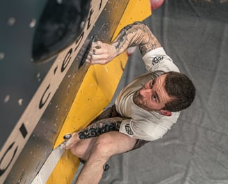 Grimpeur concentré sur un mur de bloc en salle, en pleine action sur une prise