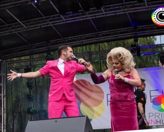 Alex in a pink suit hosting Pride in Hull. A drag queen in pink is holding his hand