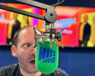Alex Duffy is in a radio studio, face half-obscured behind a Hits Radio microphone.
