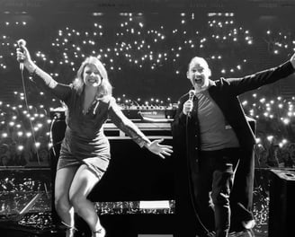 Alex Duffy and Ellie Brennan on stage in black and white in front of bright white lights from phones