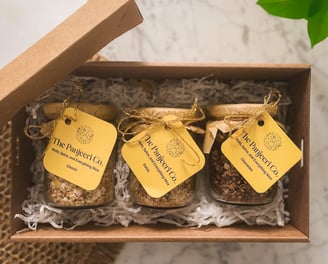 A gift box containing three glass jars of Panjeeri flavours: chocolate, dates, and classic