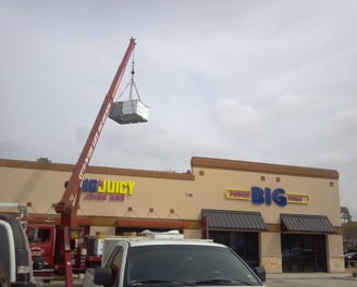 a crane is lifting a commercial A/C unit to roof