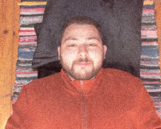 Amr El Khelawy. A man wearing a brick red jacket. Lying on the floor. Looking to the camera. Smiling
