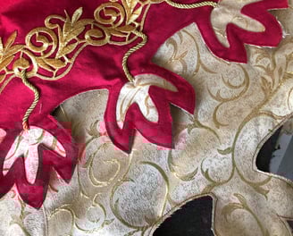 Photo de détails d'une tenue rouge et dorée avec des motifs dits de feuilles de chêne