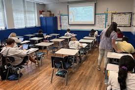 Classroom with rows of desks facing a screen where students are seated individually during a whole-g