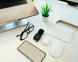 a computer monitor, keyboard, mouse, earpods, glasses, a plant showing the use of digital products