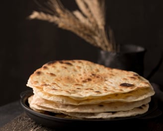 Pão sírio caseiro, fresquinho e macio, com textura levemente dourada, disposto em uma tábua rústica.